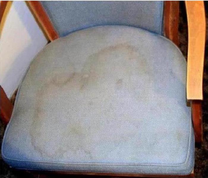 Water damage stain on the seat of a blue chair. Damaged spot is brownish and discolored from original chair color.